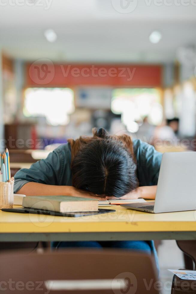 Exhausted Student Asleep on Desk with Laptop and Books in a Classroom Setting photo