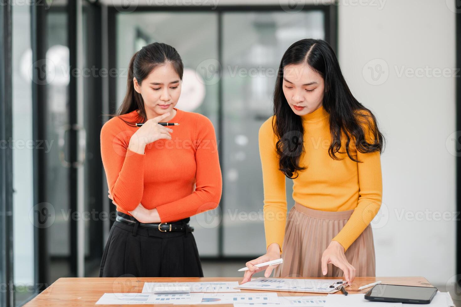 Two Young Women Collaborating on Business Project in Modern Office Setting with Documents and Digital Tablet photo