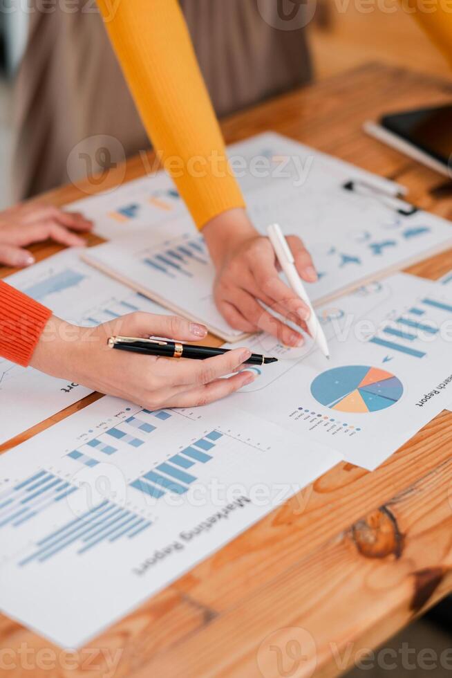 Collaborative Teamwork Analyzing Business Reports with Graphs and Charts on Wooden Desk in Modern Office Setting photo