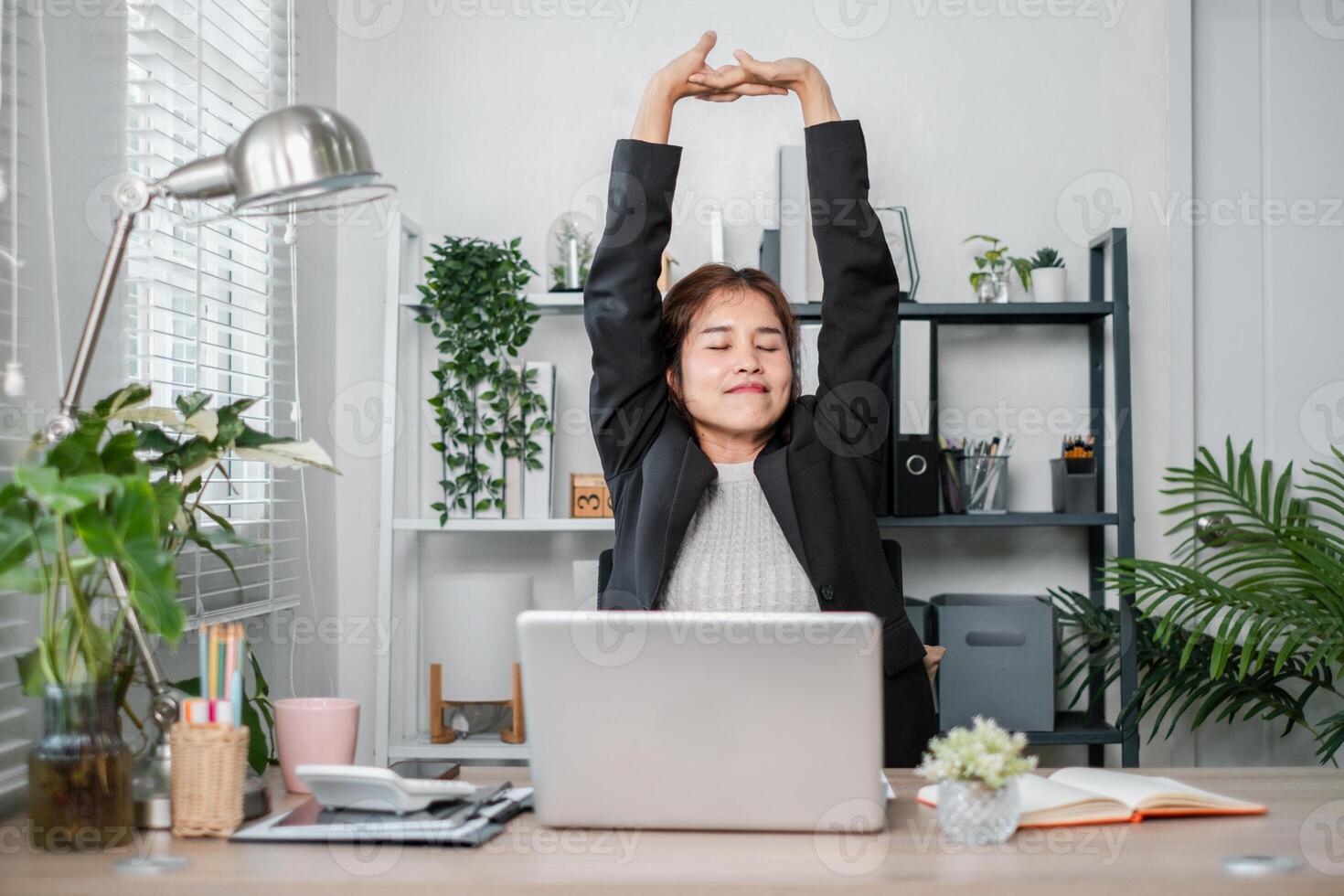 Relaxed Businesswoman Stretching at Desk in Modern Home Office with Plants and Laptop photo