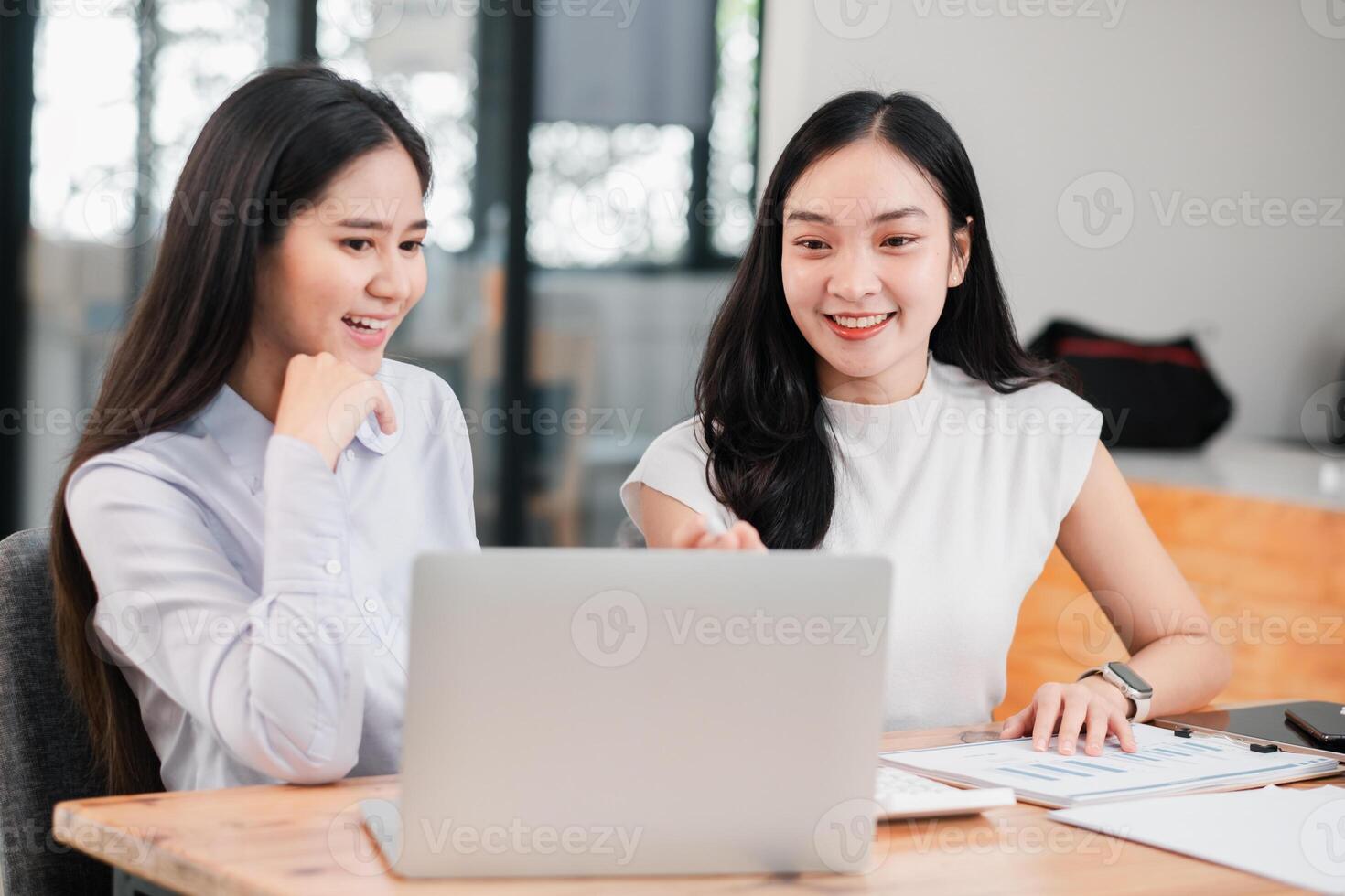 Two young women working together in a modern office, discussing ideas and using a laptop for their project. photo