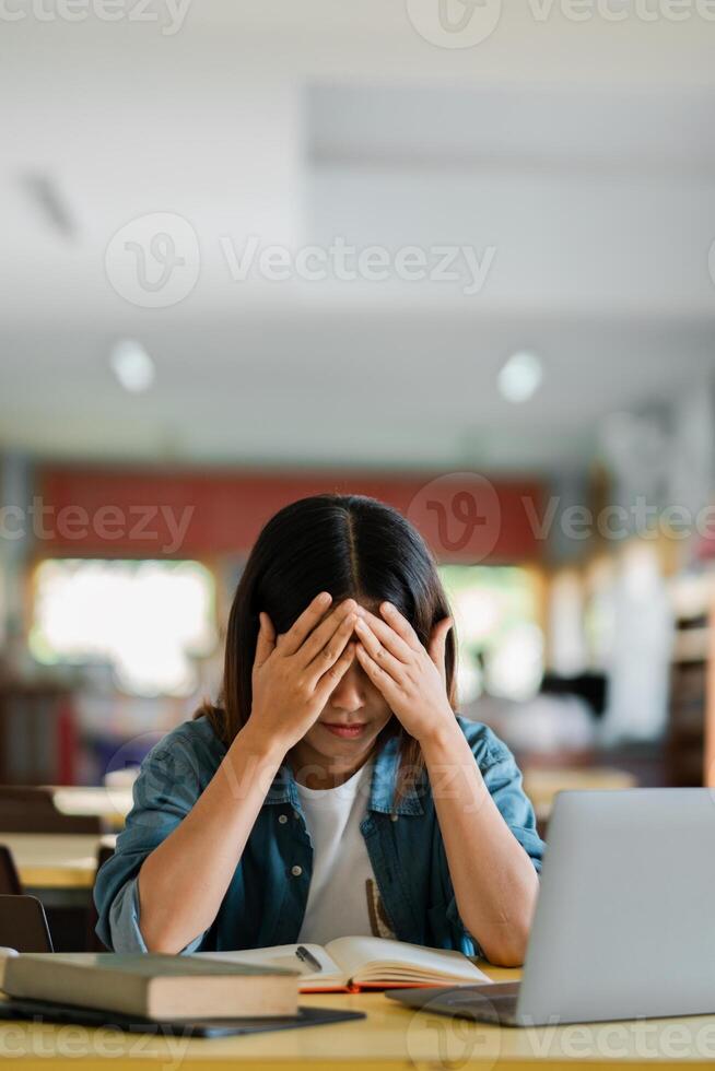 Stressed Student Studying in Library with Laptop and Books, Overwhelmed by Academic Pressure and Deadlines photo