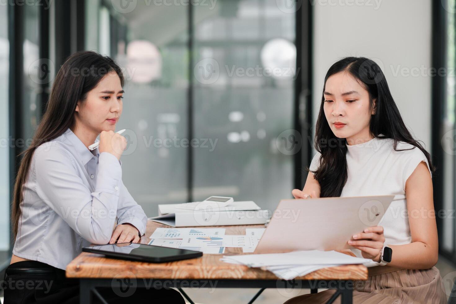 Professional Business Meeting Between Two Women Analyzing Documents in a Modern Office Setting with Technology and Charts photo