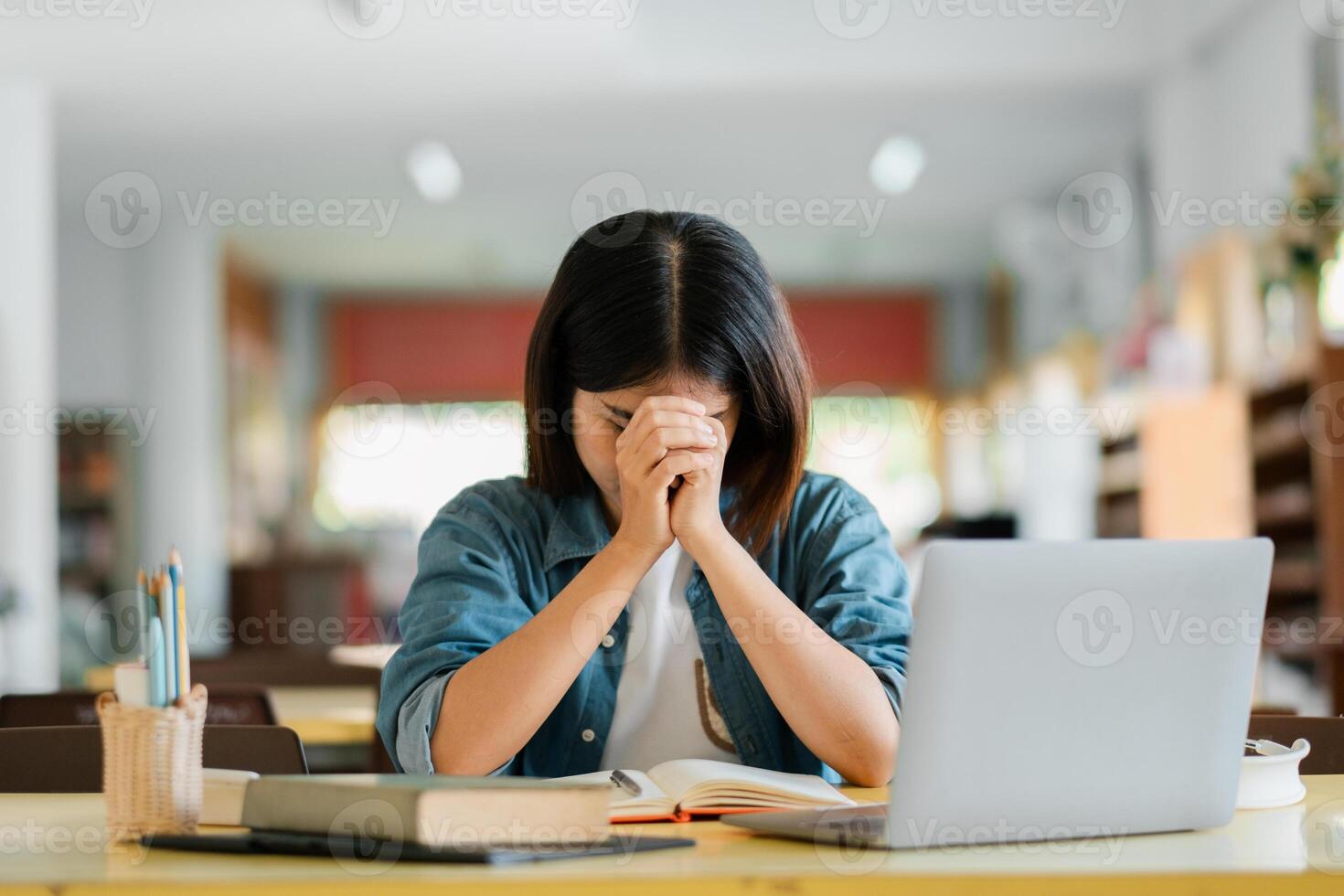 A student in a library feeling stressed while studying with a laptop and books, symbolizing academic pressure and the pursuit of knowledge. photo