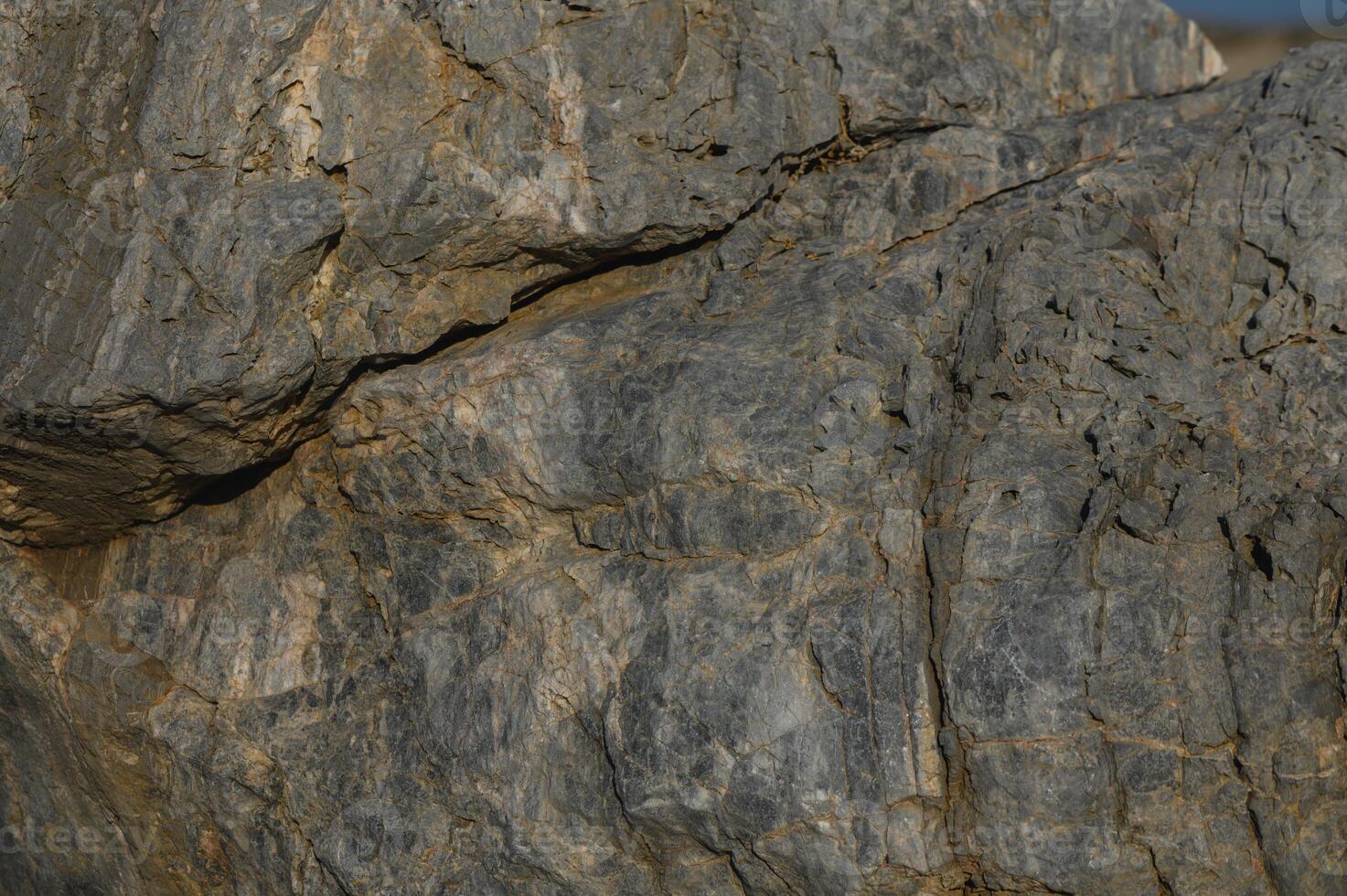 Textured surfaces of a large rock formation glistening in the sun beside a serene ocean backdrop. photo