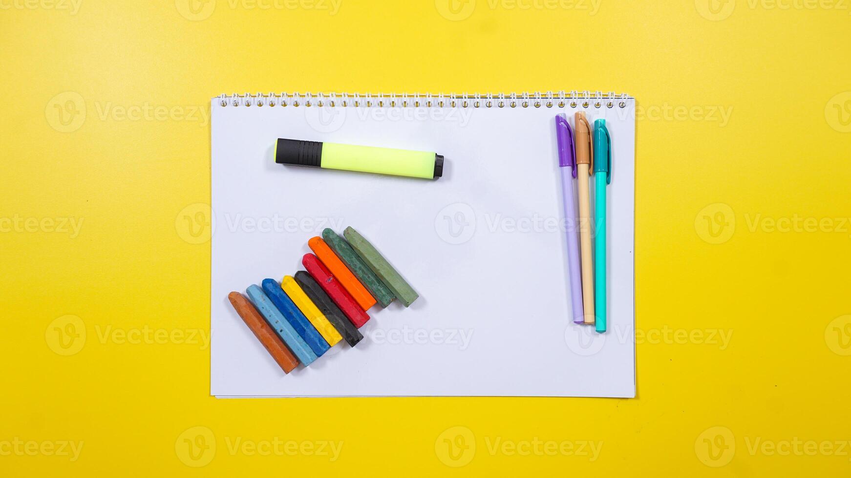 Pens, Crayons and Highlighter Above The Notebook Isolated on Yellow Background photo