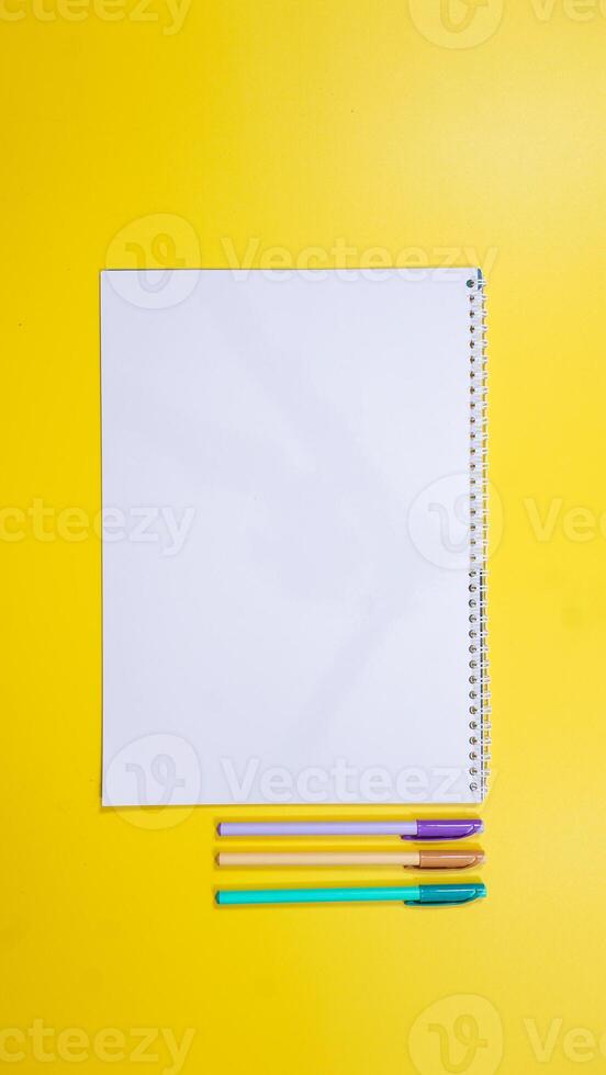 Blank Notebook for Copy Space with Pens Isolated on Yellow Background photo
