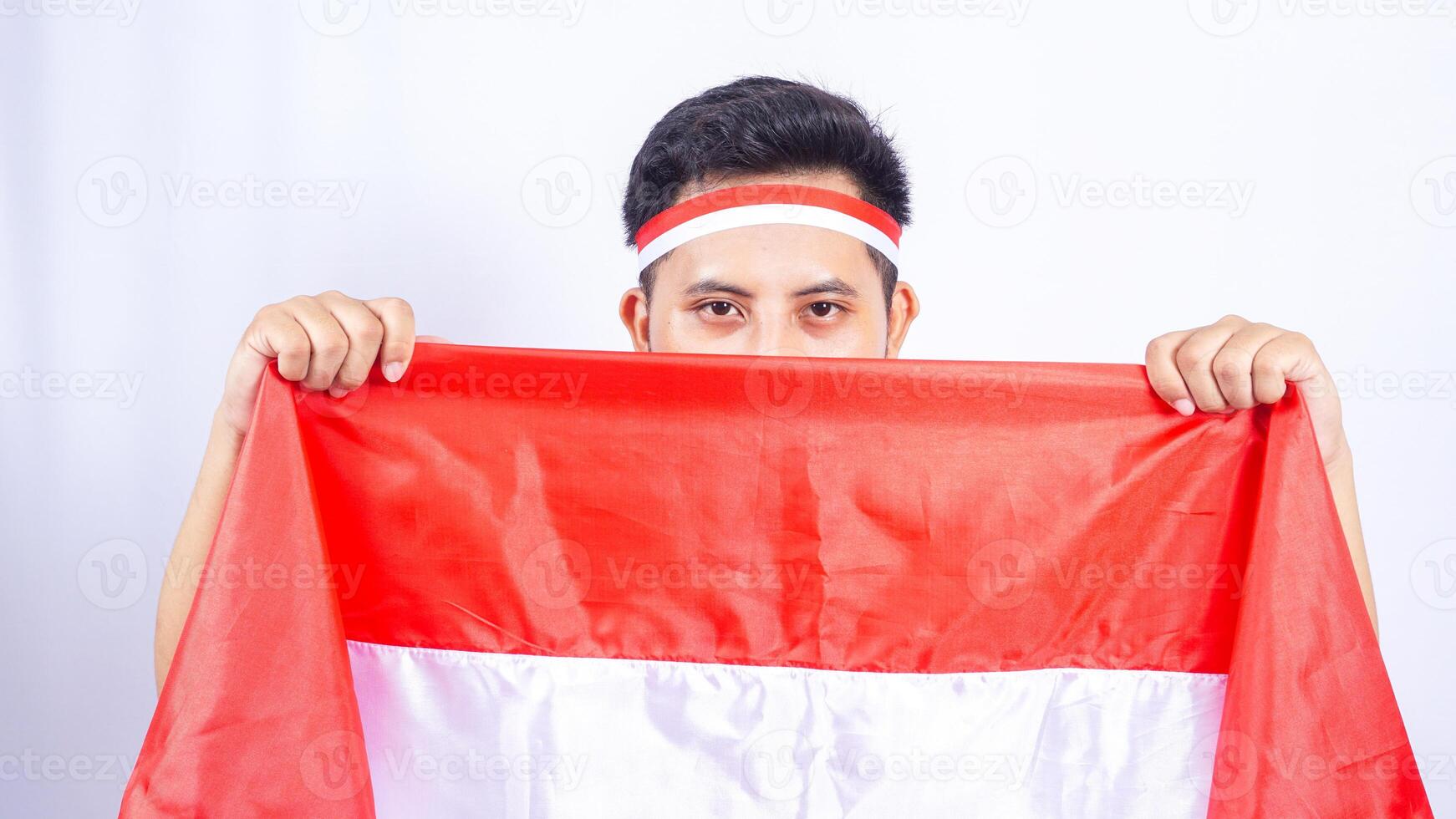 Young Indonesian Man Covering Face with Red and White Colored Flag of Indonesia photo