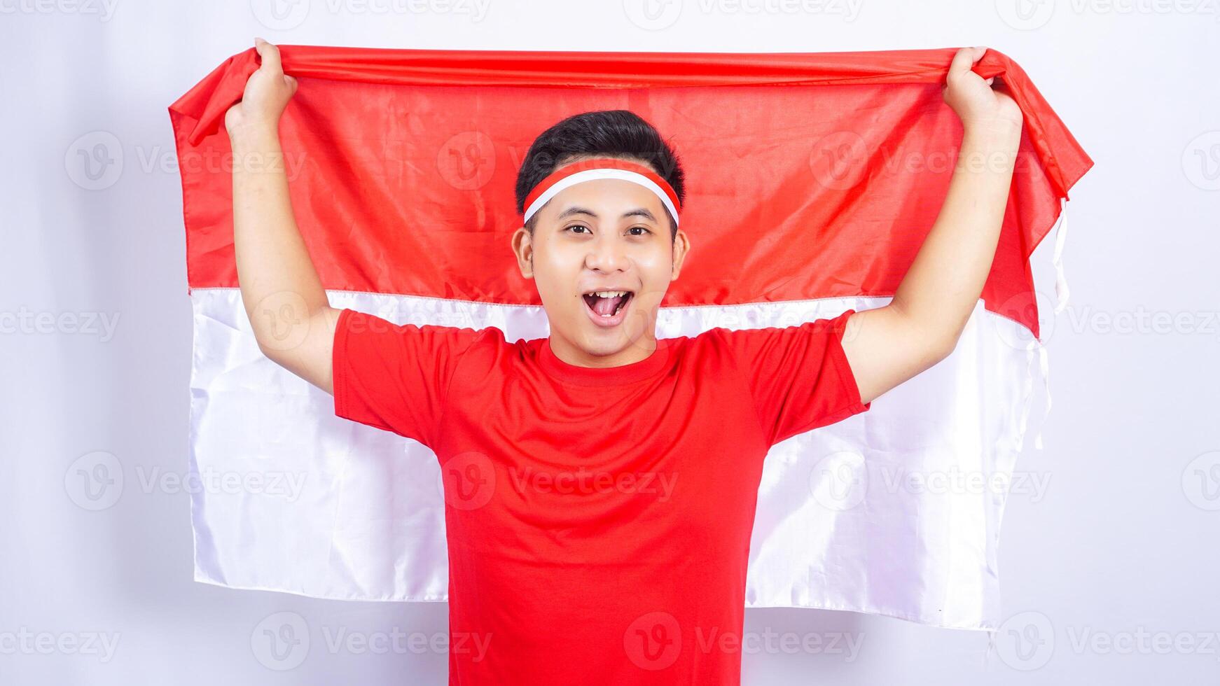 Excited Young Indonesian Man Holding Wide Open Indonesia Flag Behind Back photo