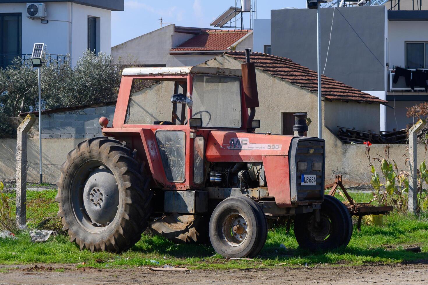 Gaziveren Cyprus -25.01.2025 Old red tractor resting by the fence in a rural landscape under a clear blue sky photo