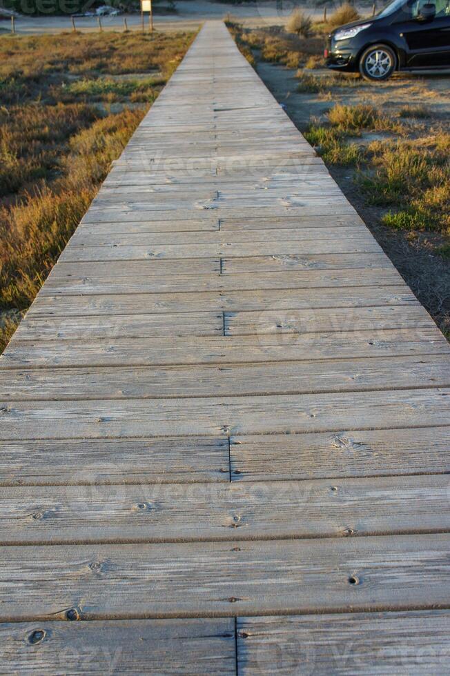 A serene wooden walkway stretches through grassy terrain at sunset beside a parked vehicle. photo
