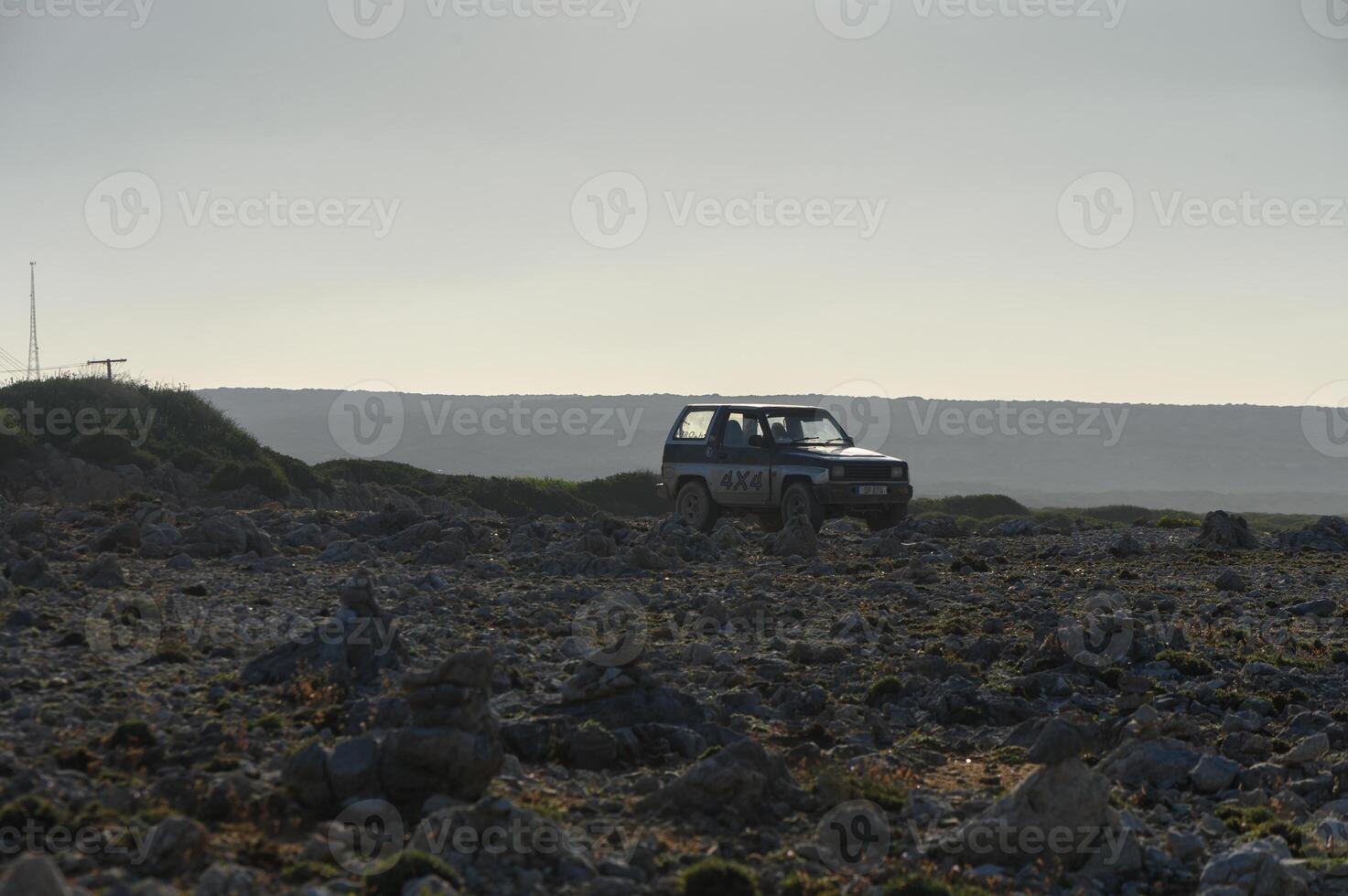A lone vehicle navigates the rocky terrain under the expansive, cloudy sky at dusk. photo