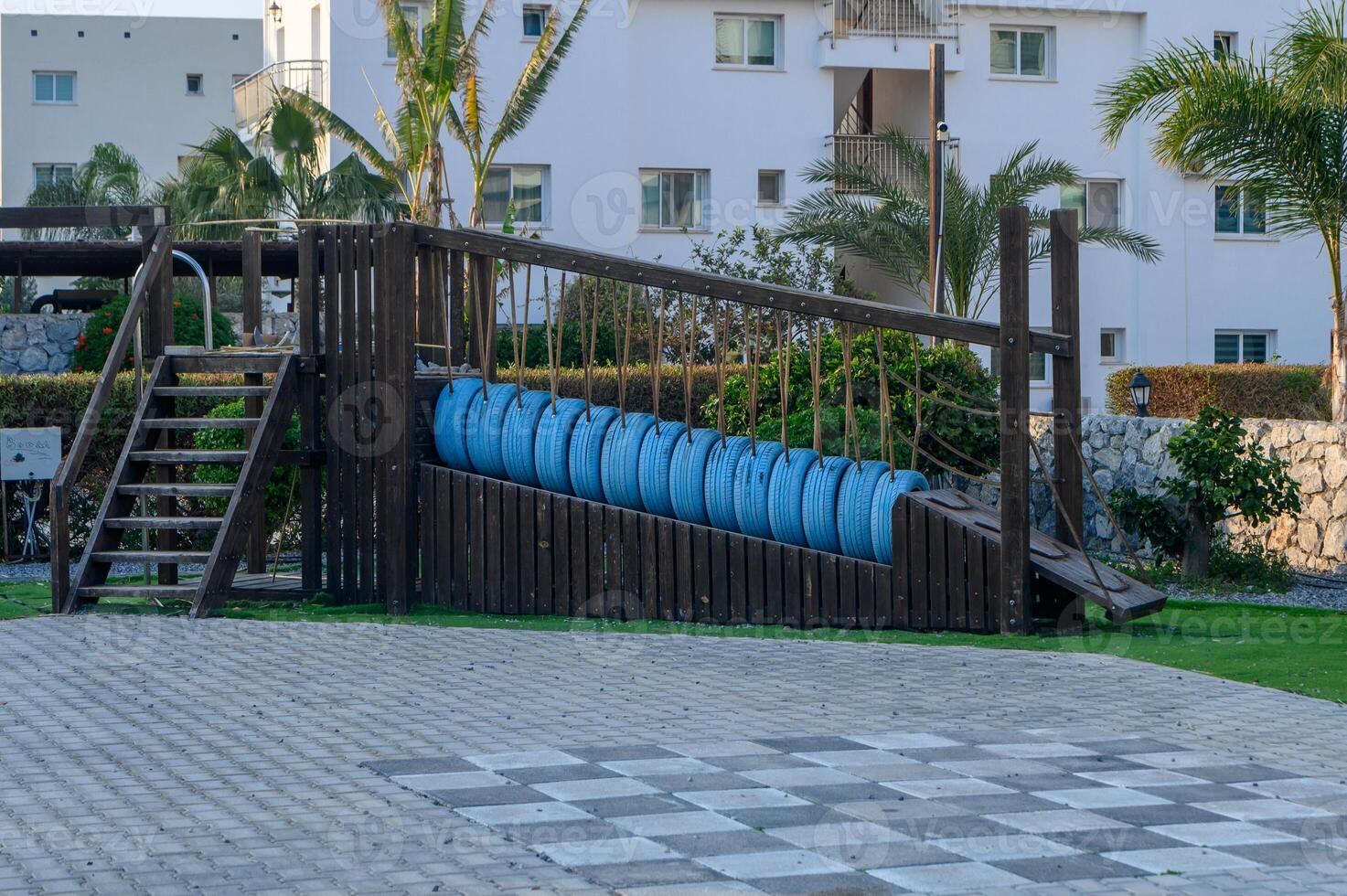 Playground structure featuring bright blue swings in a serene family-friendly park with palm trees photo