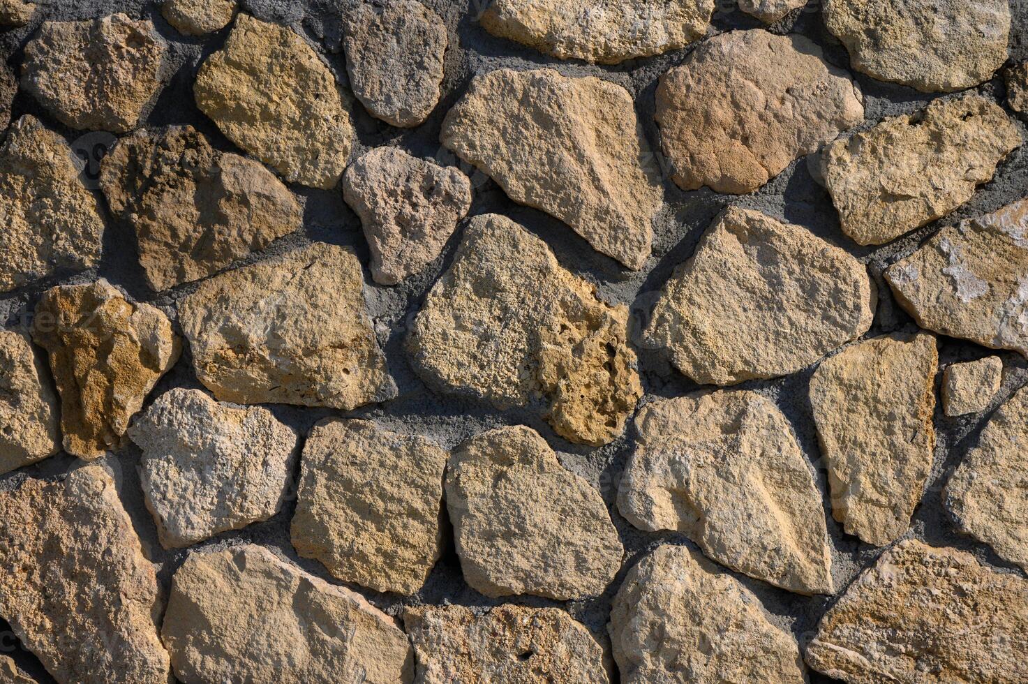 Natural stone wall crafted from assorted rocks in warm hues under bright sunlight photo