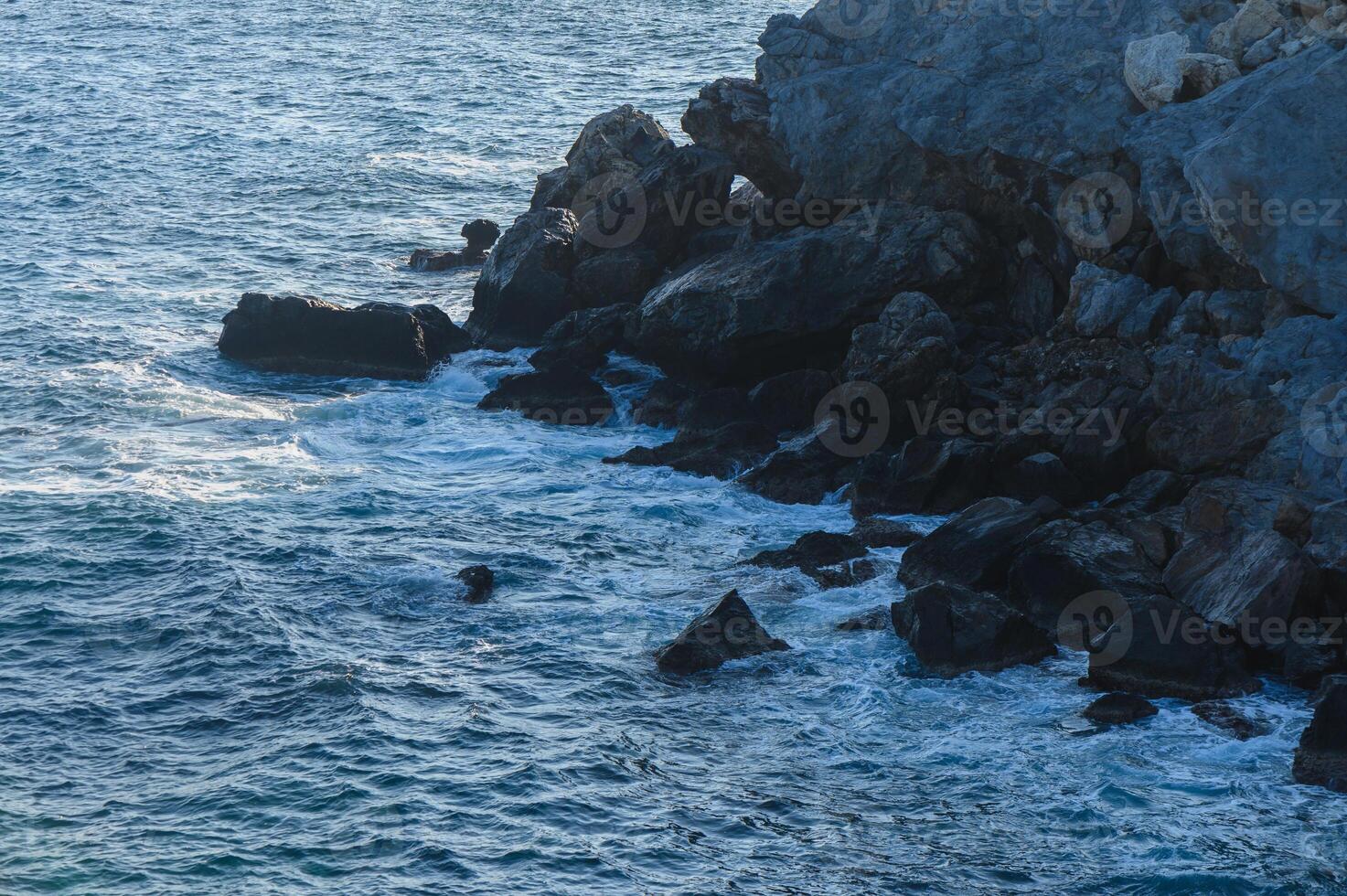 Waves crashing against rugged coastal rocks at twilight along the serene seashore. photo