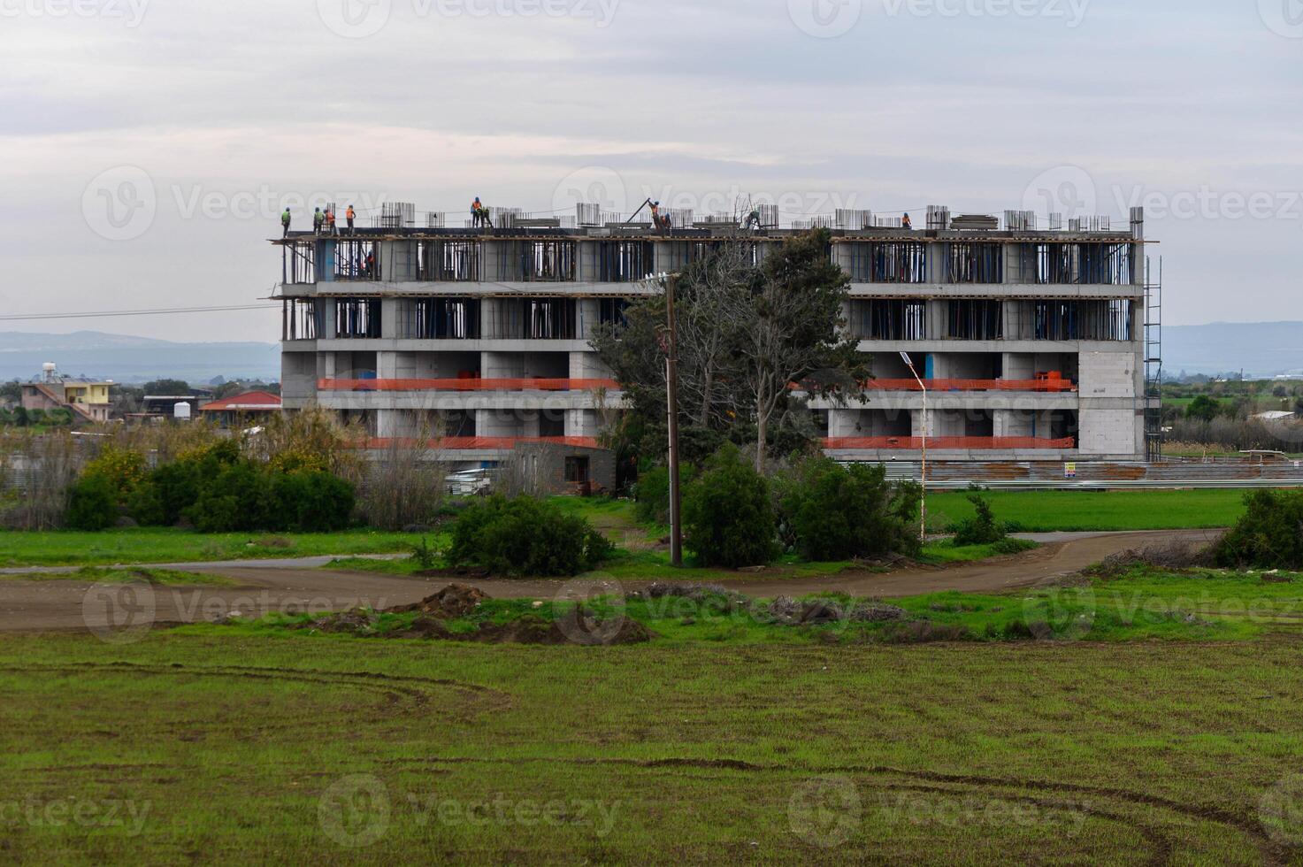 Construction workers diligently build a large modern structure in a rural area under overcast skies photo