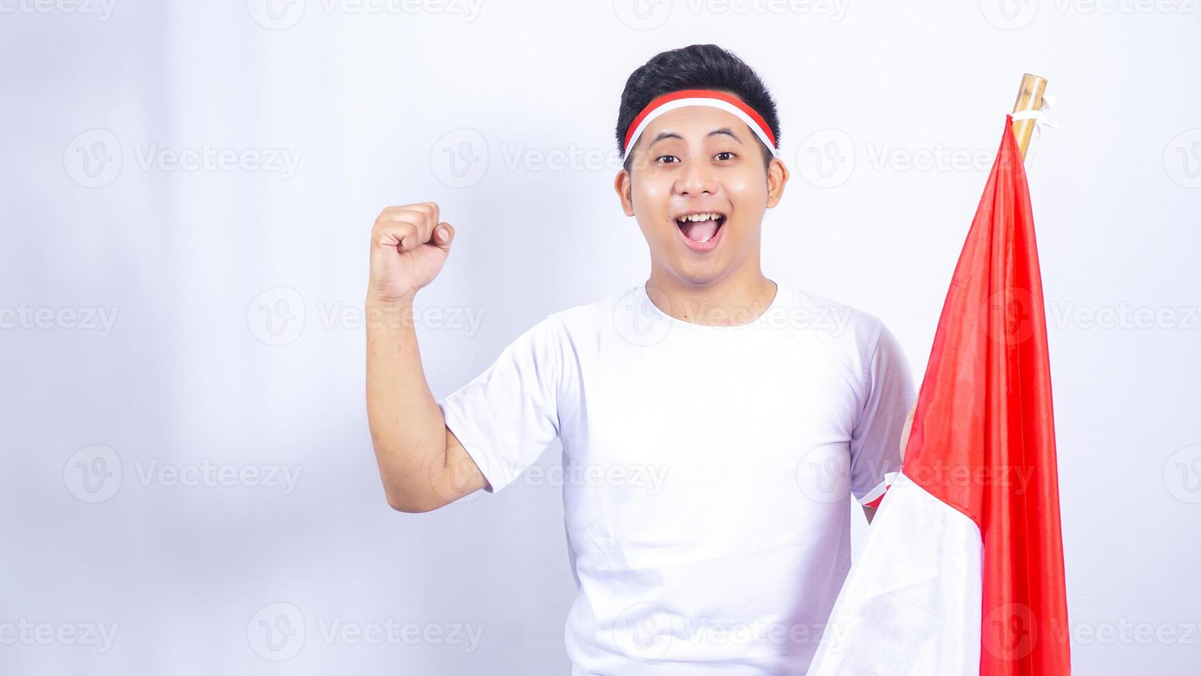 Excited Indonesian Young Man Raising Fist while Holding Country Flag photo