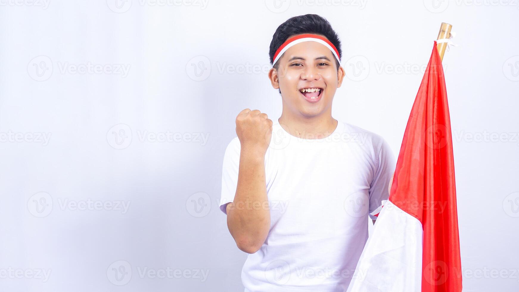 Excited Indonesian Young Man Raising Fist while Holding Country Flag Isolated on White Background photo
