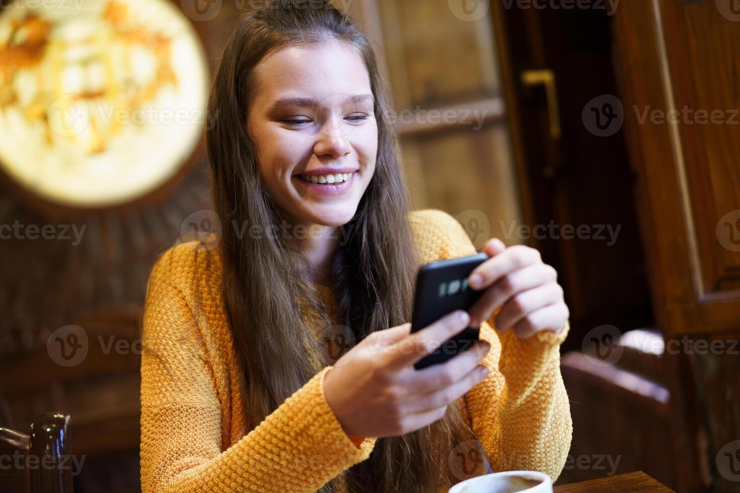 Cheerful Young Woman Relaxing and Enjoying a Tasty Coffee while Texting on Her Smartphone photo