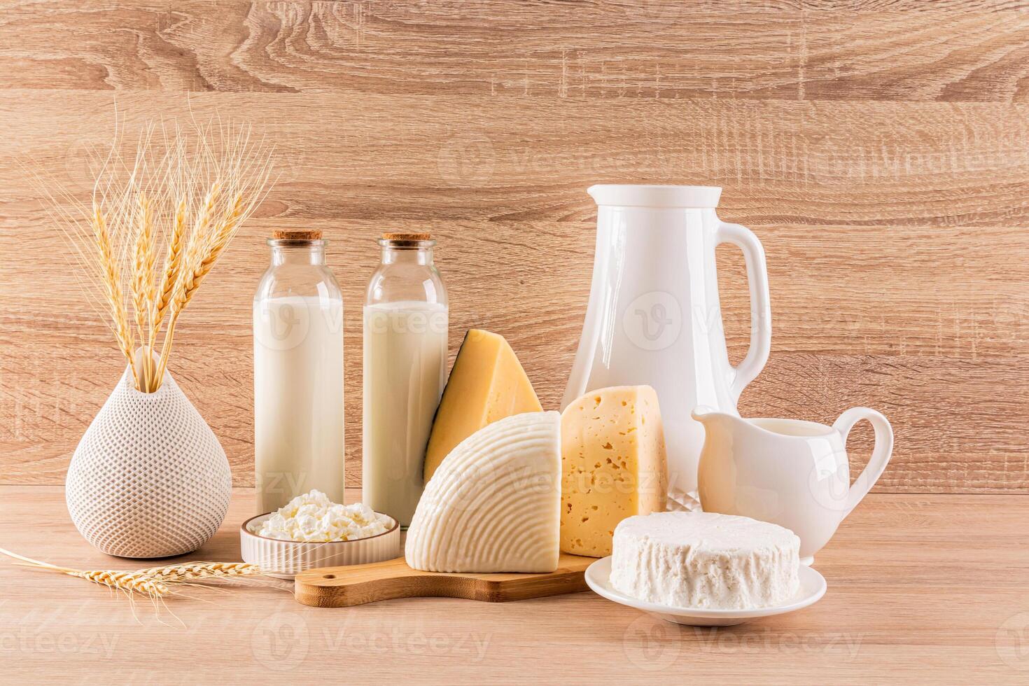 Traditional dairy products in bottles, jugs on a wooden background. a vase with ears of wheat. symbol of holiday Shavuot. Front view. Rustic style. photo