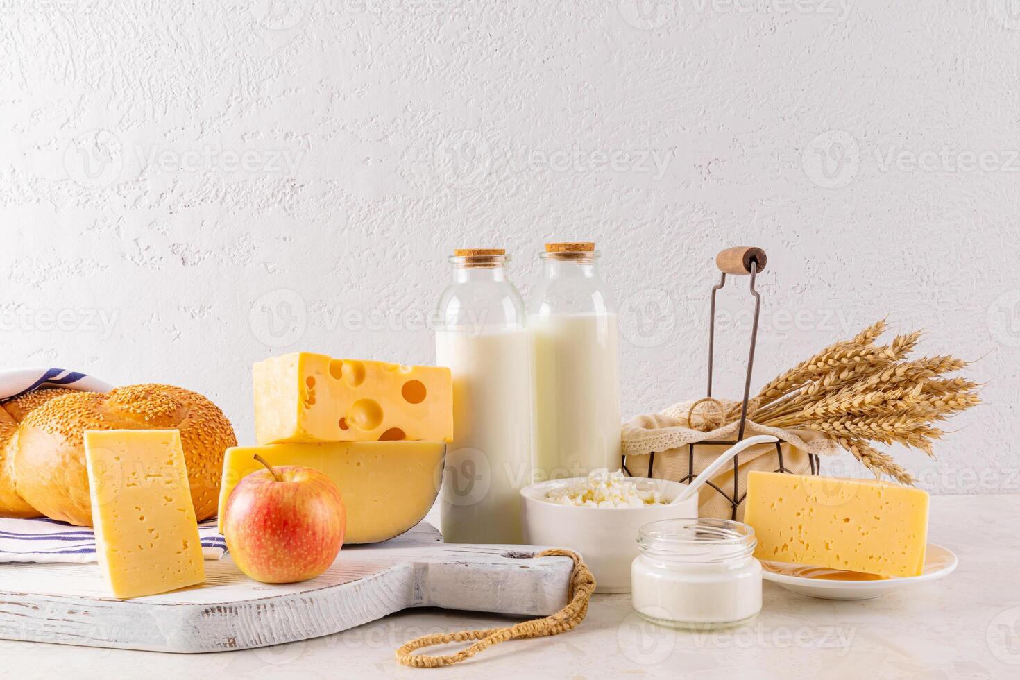Many varieties of cheese on a board, bottles of milk, cottage cheese, sour cream, a bunch of ears of bread on a light table. The holiday of Shavuot. photo