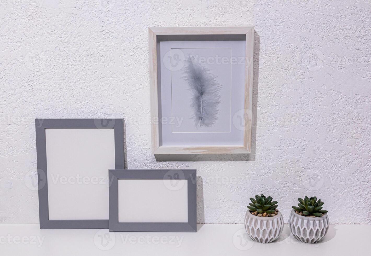 Stylish minimalist decor in light colors on a white table in a modern space. Two gray photo frames, a painting, pots. Front view. eco items.