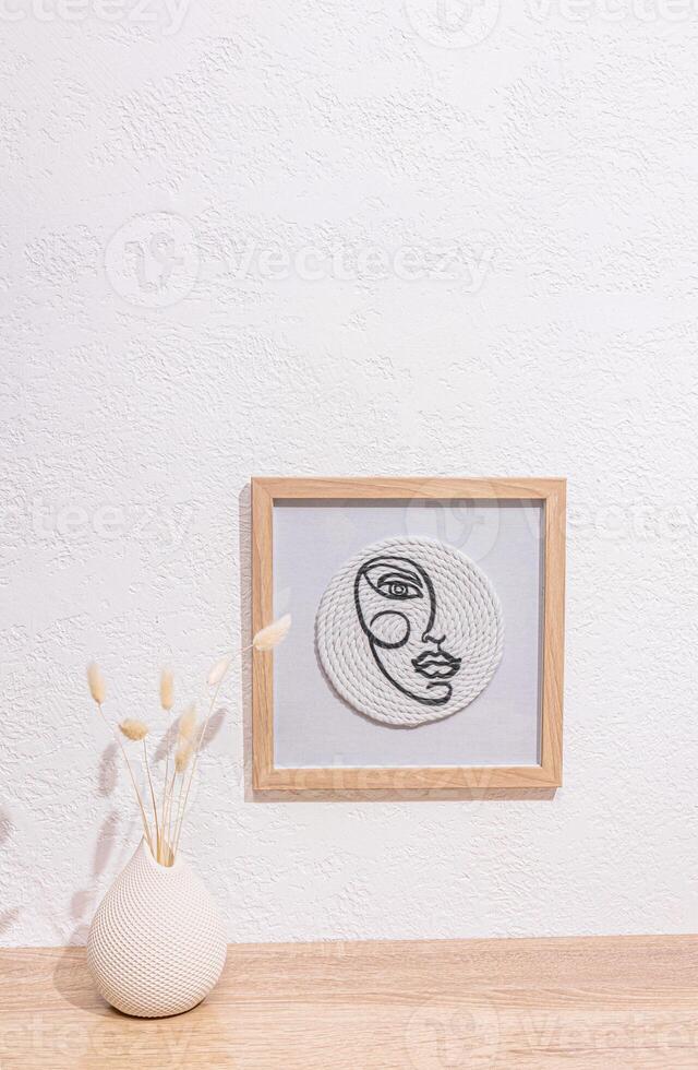 A stylish modern painting on the white surface of a table or chest of drawers with a vase of dried flowers. home decor in white tones. Vertical view. photo