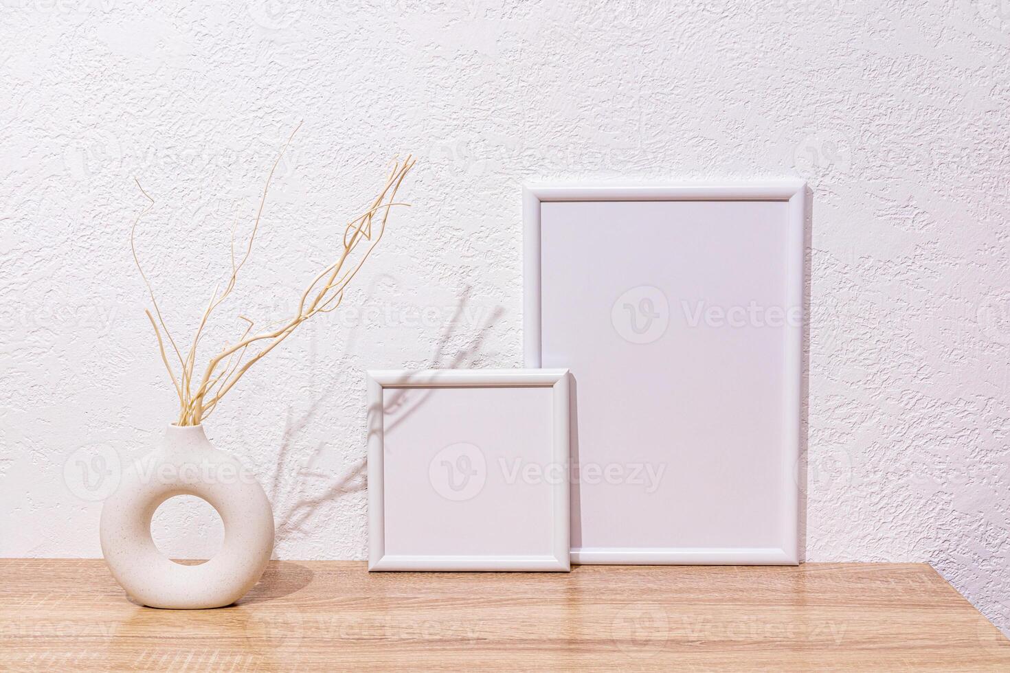 Home decor elements in a light style with white photo frames, a vase made of natural material with dry tree branches on wooden countertop. Front view