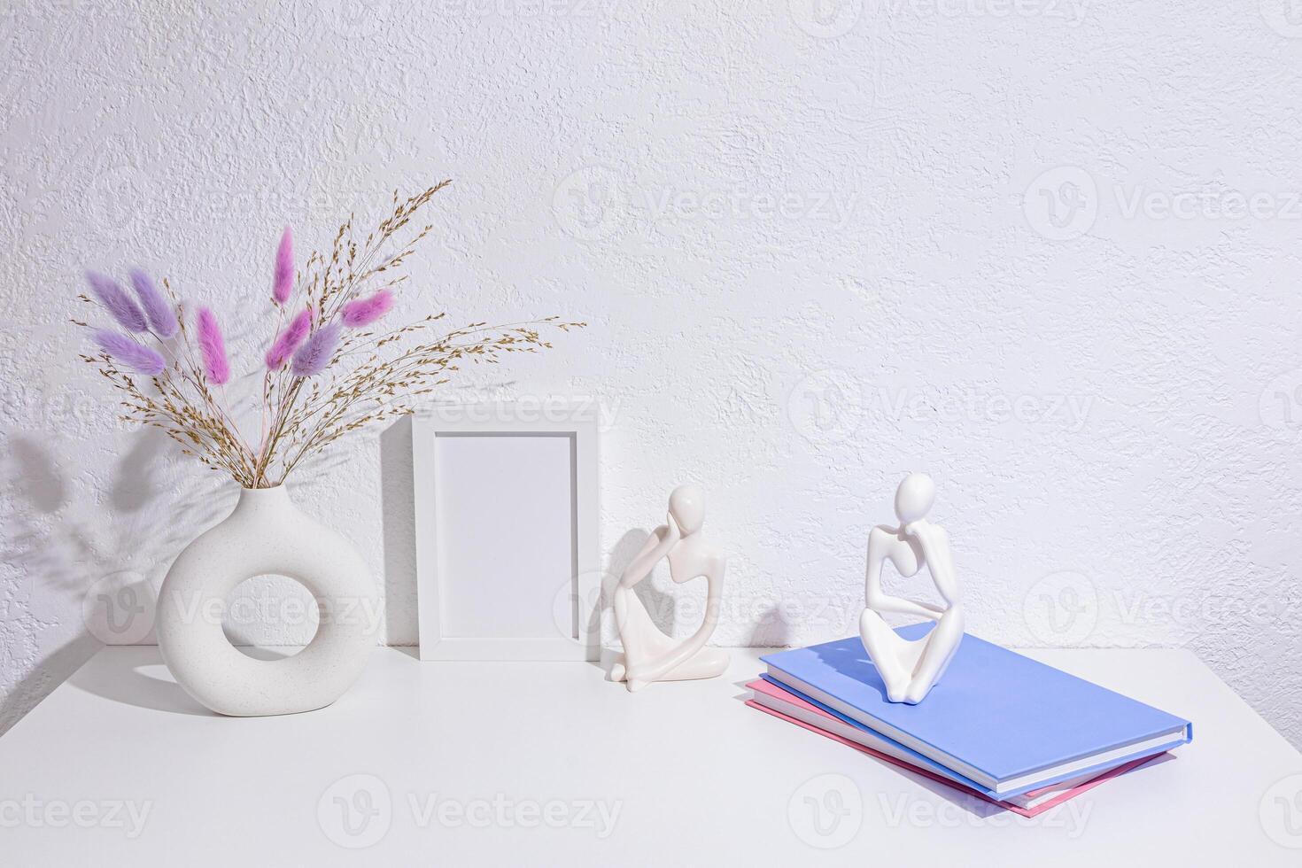 Beautiful decorative objects on a white table in the interior of a modern space. A photo frame, lilac dried flowers in stylish vase, statuette, books.