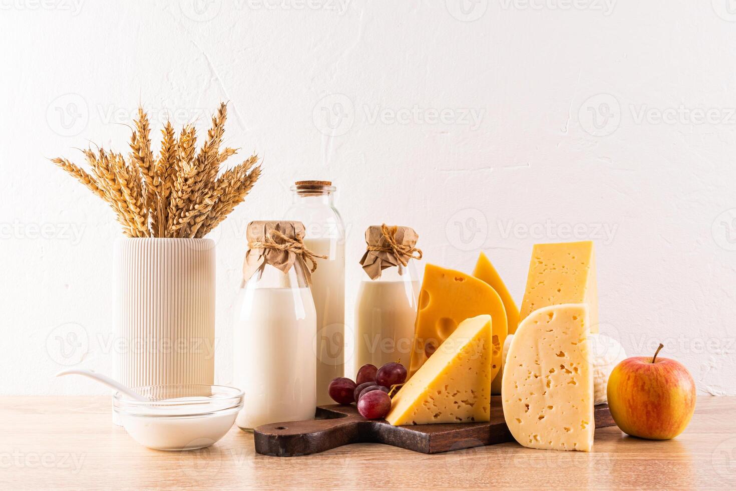 cheese, bottles of milk, grapes, an apple, a vase with ears of wheat on a wooden table. Traditional treats and symbols of the Shavuot. Front view. photo