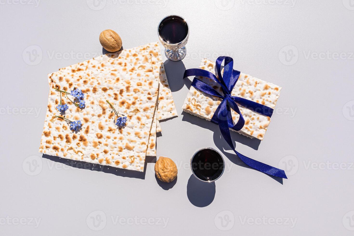 Festive composition of the Passover. matzah, silver glasses with red wine, walnuts on light background. a shot of matzah with a blue ribbon. top view photo