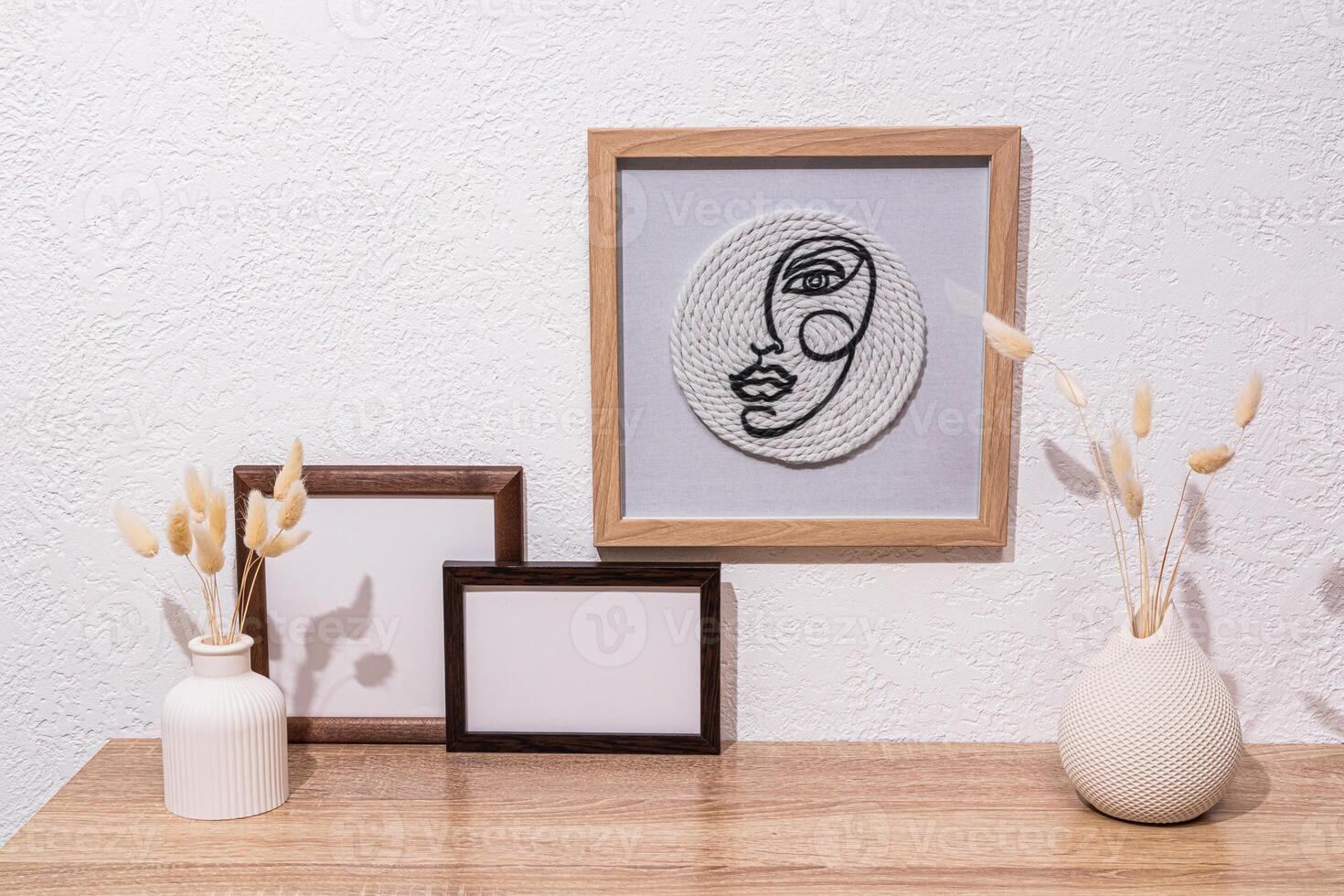 design elements of a modern room. stylish ceramic vases with dried flowers, photo frames, a framed painting on a white textured wall. Front view