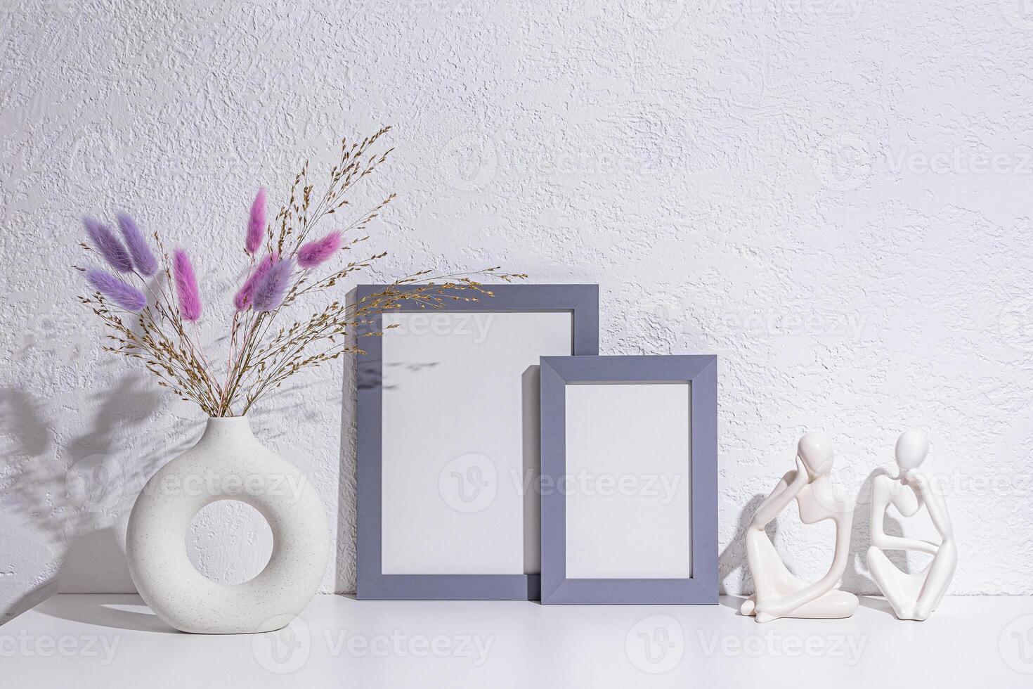 decorative objects on a white table in the interior of a modern space. A photo frame, lilac dried flowers in stylish vase, statuette. Front view.
