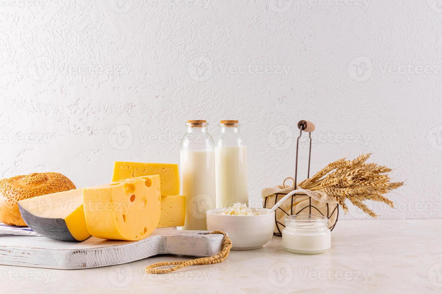 various types of cheese on a white wooden board, bottles of milk, ears of bread on a wooden table. The concept of the Shavuot holiday. Front view. photo