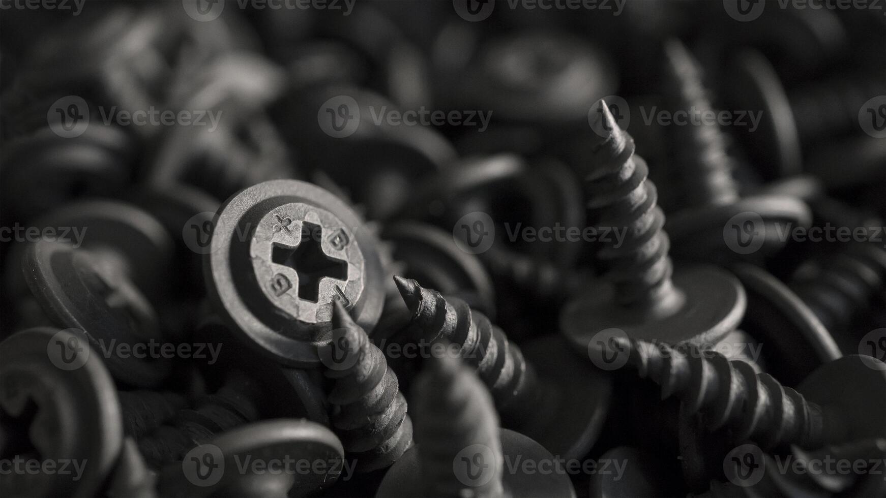 A detailed macro shot of black drywall screws for metal studs with cross-shaped heads arranged in a dense pile. Monochromatic image of drywall screws suitable for industrial or mechanical backgrounds. photo