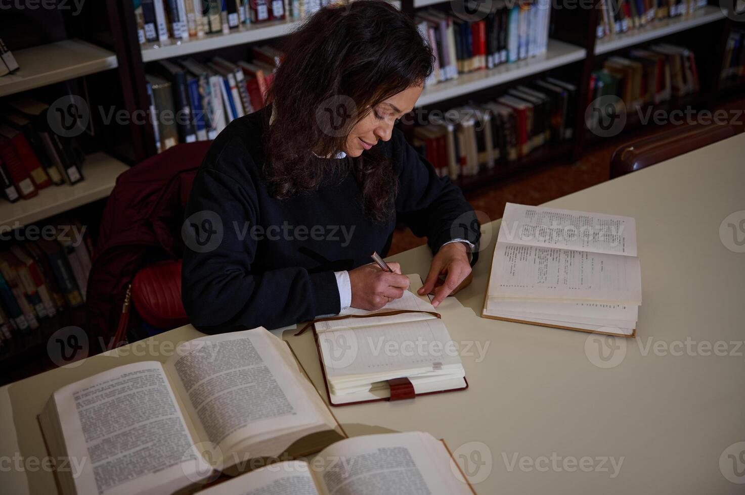Student studying and taking notes in a library while reading books photo