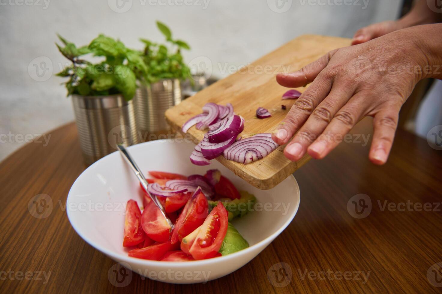 Person preparing a fresh vegetable salad on a wooden surface photo