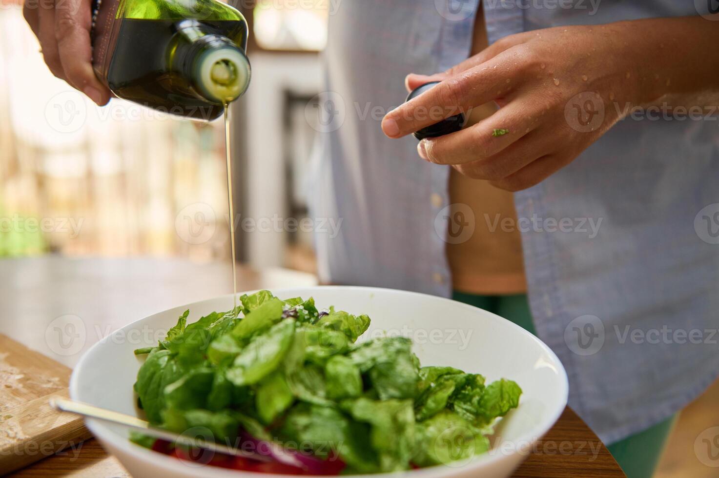 Person Pouring Olive Oil Over Fresh Green Salad in Bright Home Kitchen photo