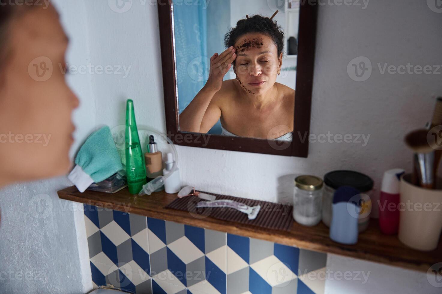 Woman applying a facial mask in front of a mirror in her bathroom photo