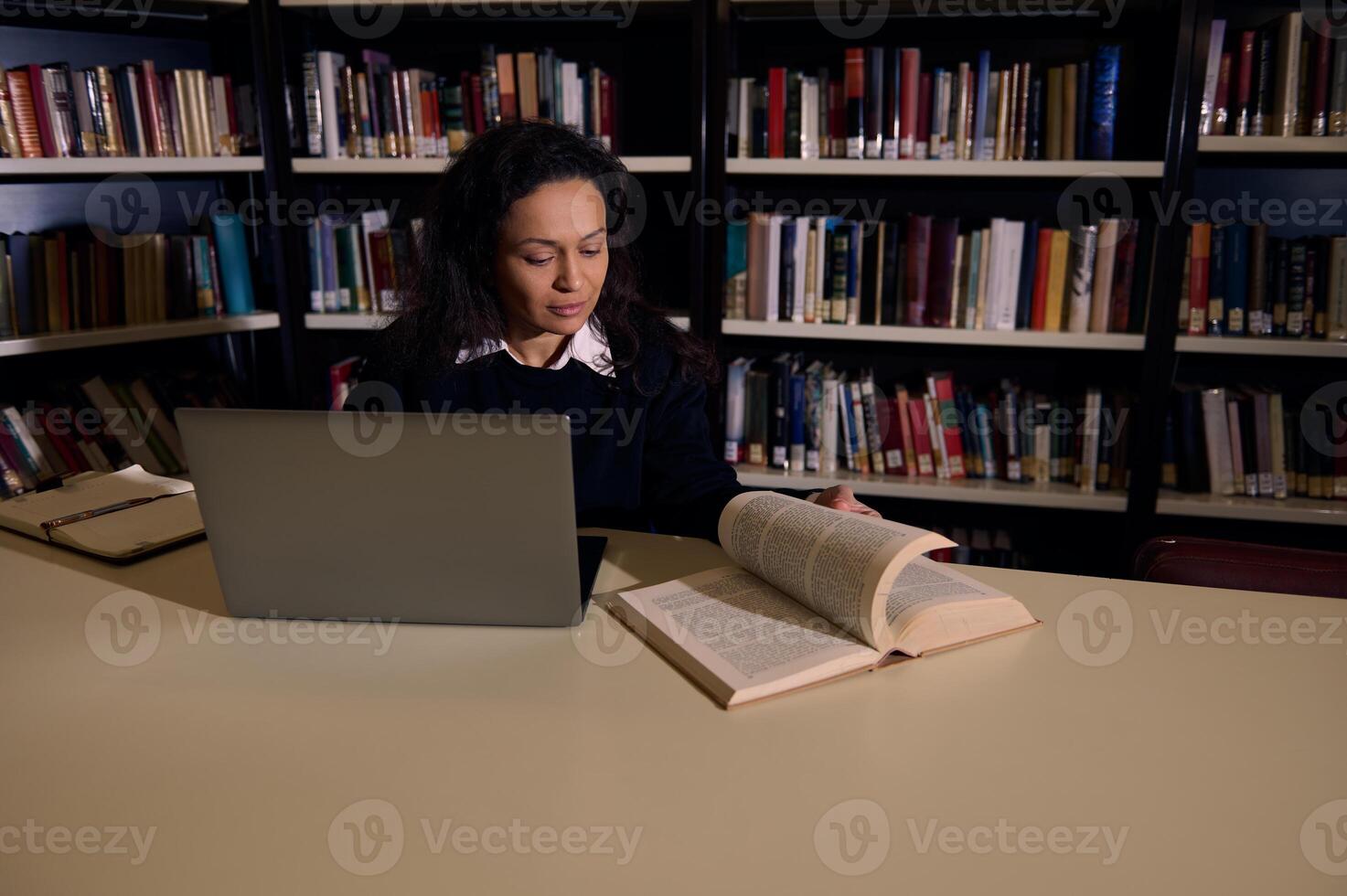 Woman Studying in a Library with a Laptop and Open Book photo