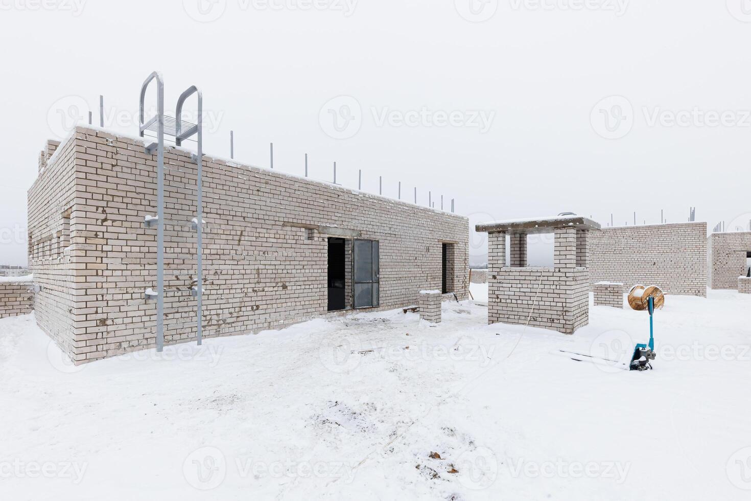 Winters Pause A Brick Building Emerges Amidst the Snowy Silence, Surrounded by Tools and Materials Awaiting the Craftsmans Touch. photo