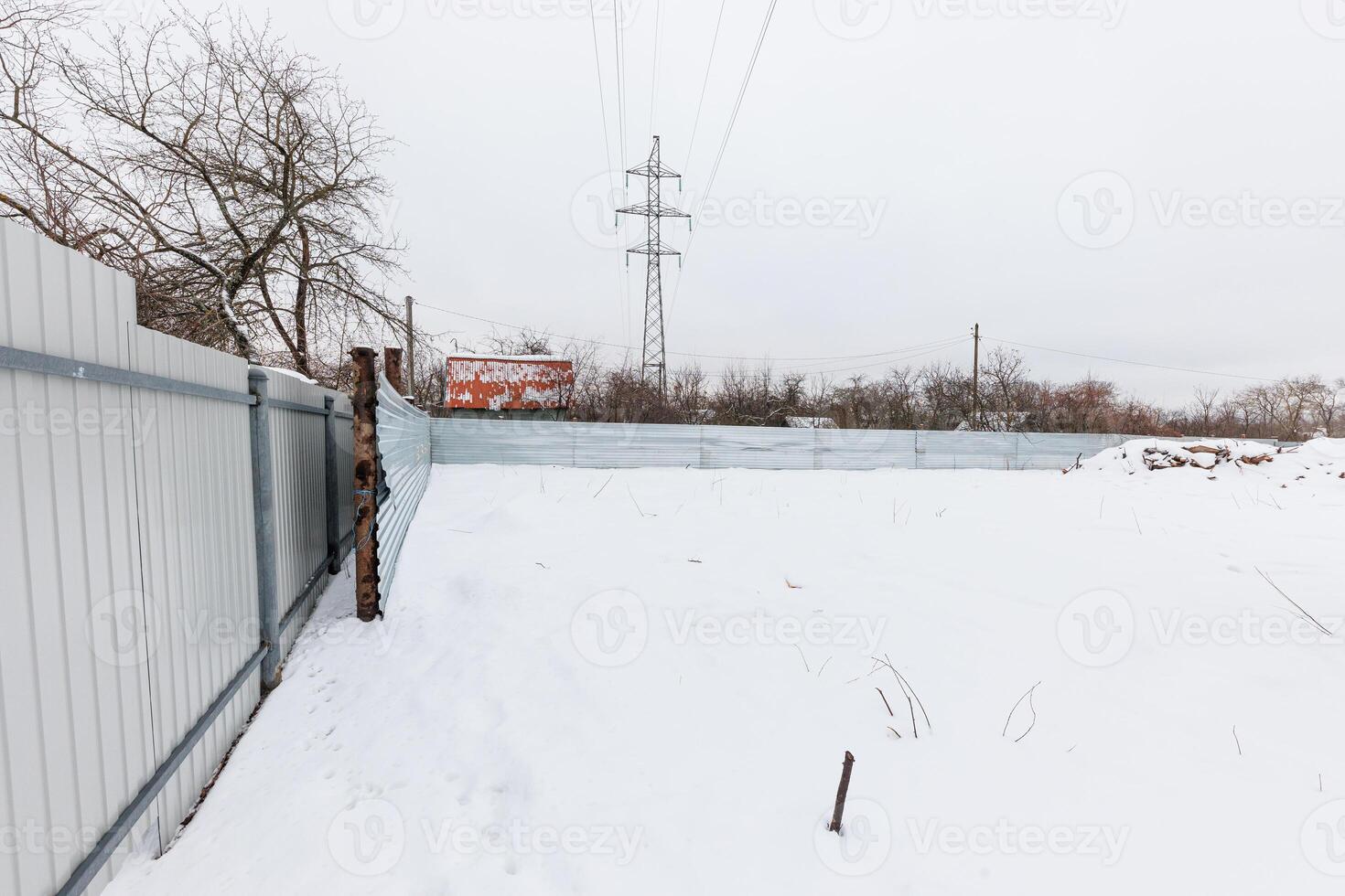Silent Winter Escape A desolate snowy lot enclosed by metal, under a moody sky, whispers stories of solitude amidst barren trees and wiry power lines. photo
