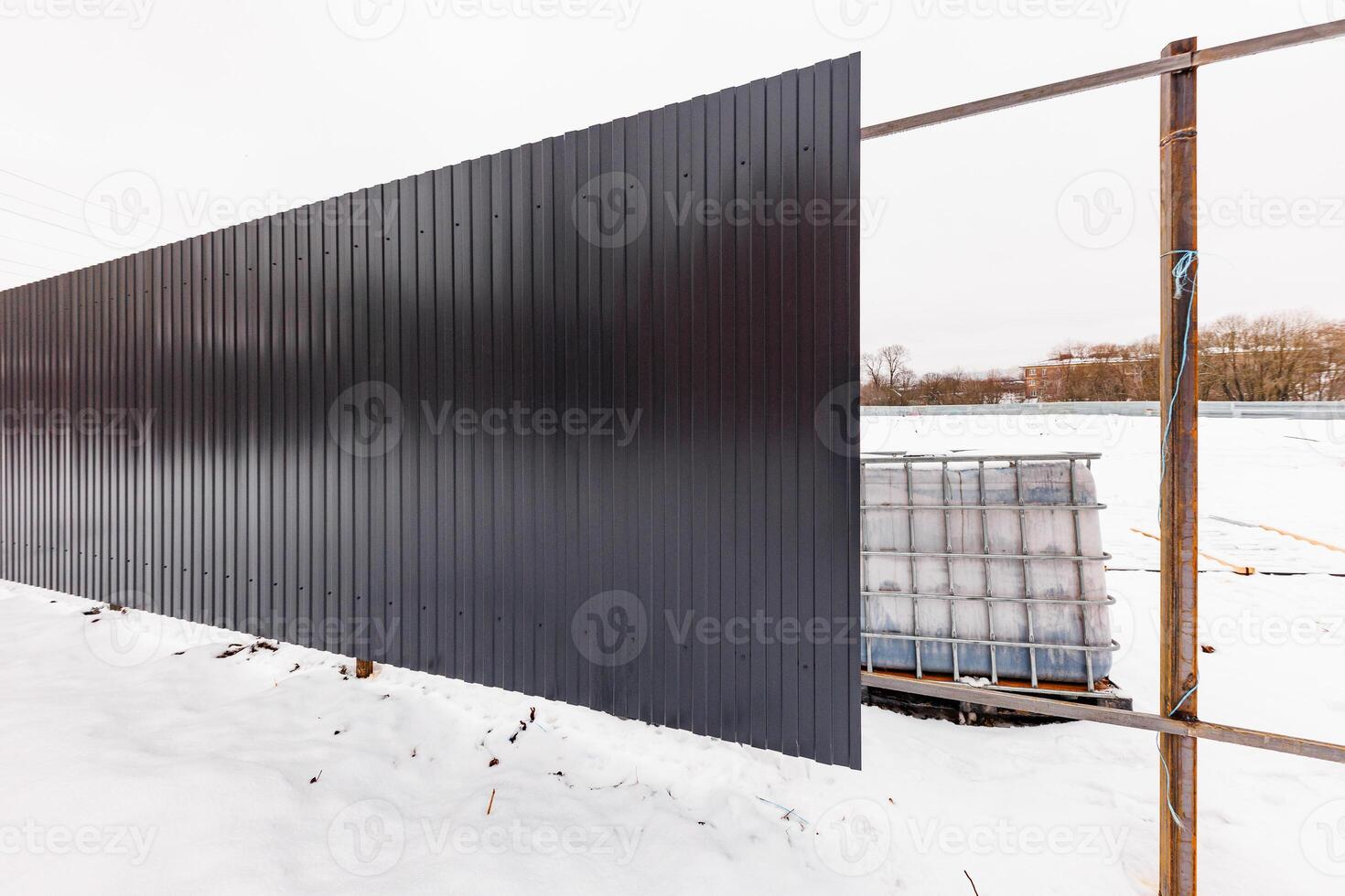 Winters Barrier A Partially Constructed Metal Fence Guarding Stacked IBC Containers Amidst a Snowy Landscape photo