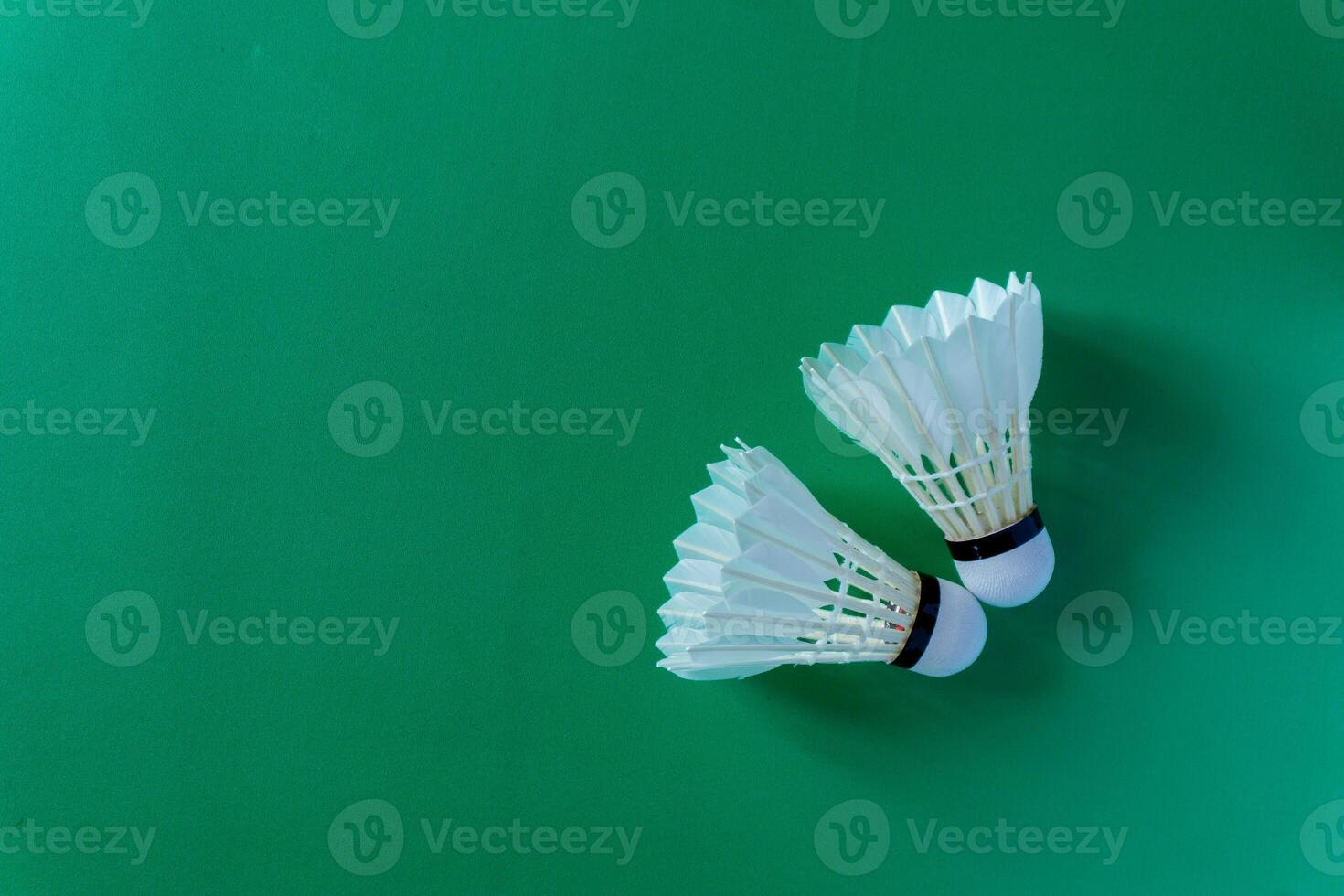 Two shuttlecocks against a green surface, copy space photo