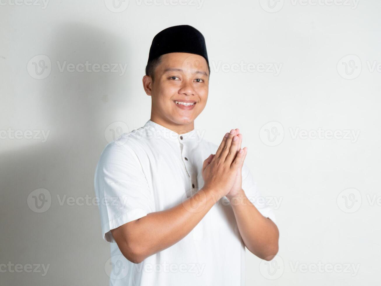 Muslim Asian man smiling and happy and shows Eid Mubarak greeting and welcoming Ramadan gesture over white background. Concept of Muslim religious people and islamic lifestyle photo