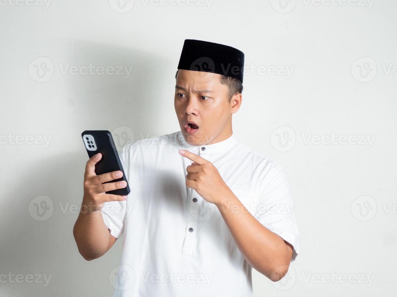 portrait of moslem Asian man shows shocked and surprised expression while holding mobile phone. photo
