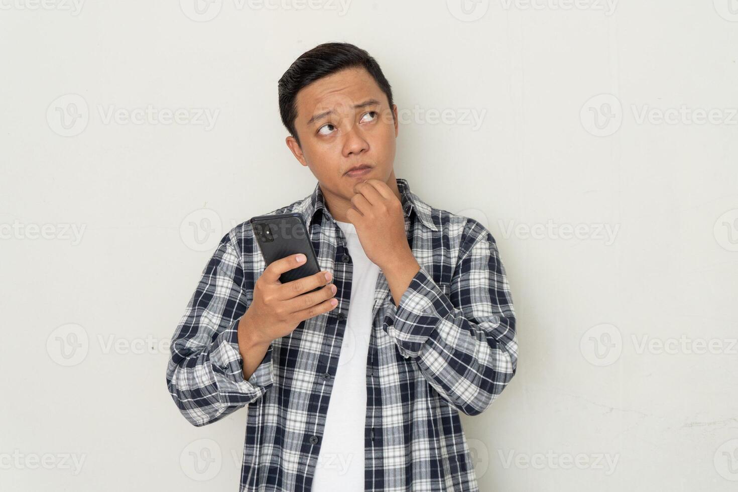 man thinking and concentrating while holding handphone. Asian student thinking and looking for ideas while holding phone photo