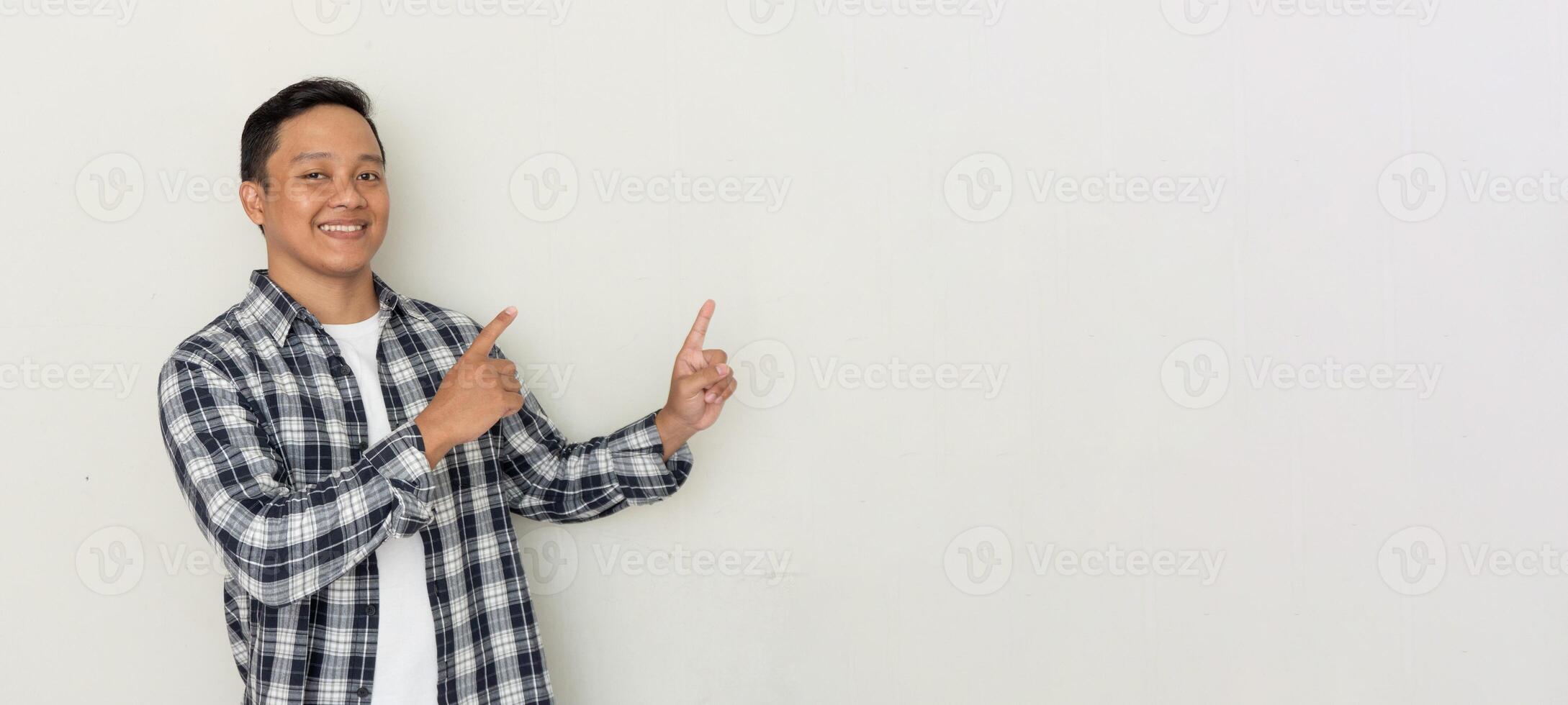 Attractive young Asian man smiling and pointing his finger to the side. Copy space. photo