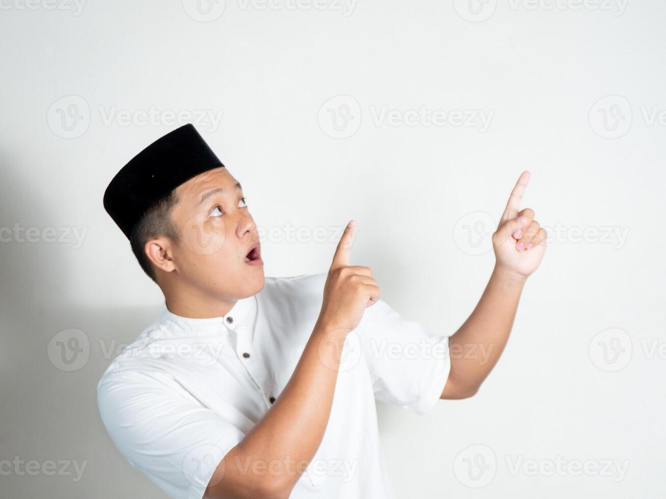 portrait of Muslim Asian man using white shirt and black cap pointing finger with shocked expression photo