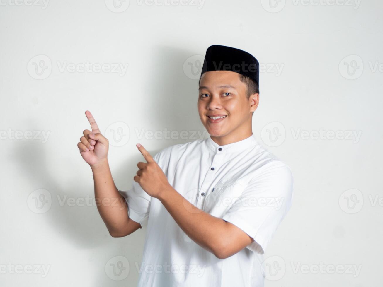 Asian man using white shirt and black cap pointing finger at free space place for an advertisement. Muslim man photo